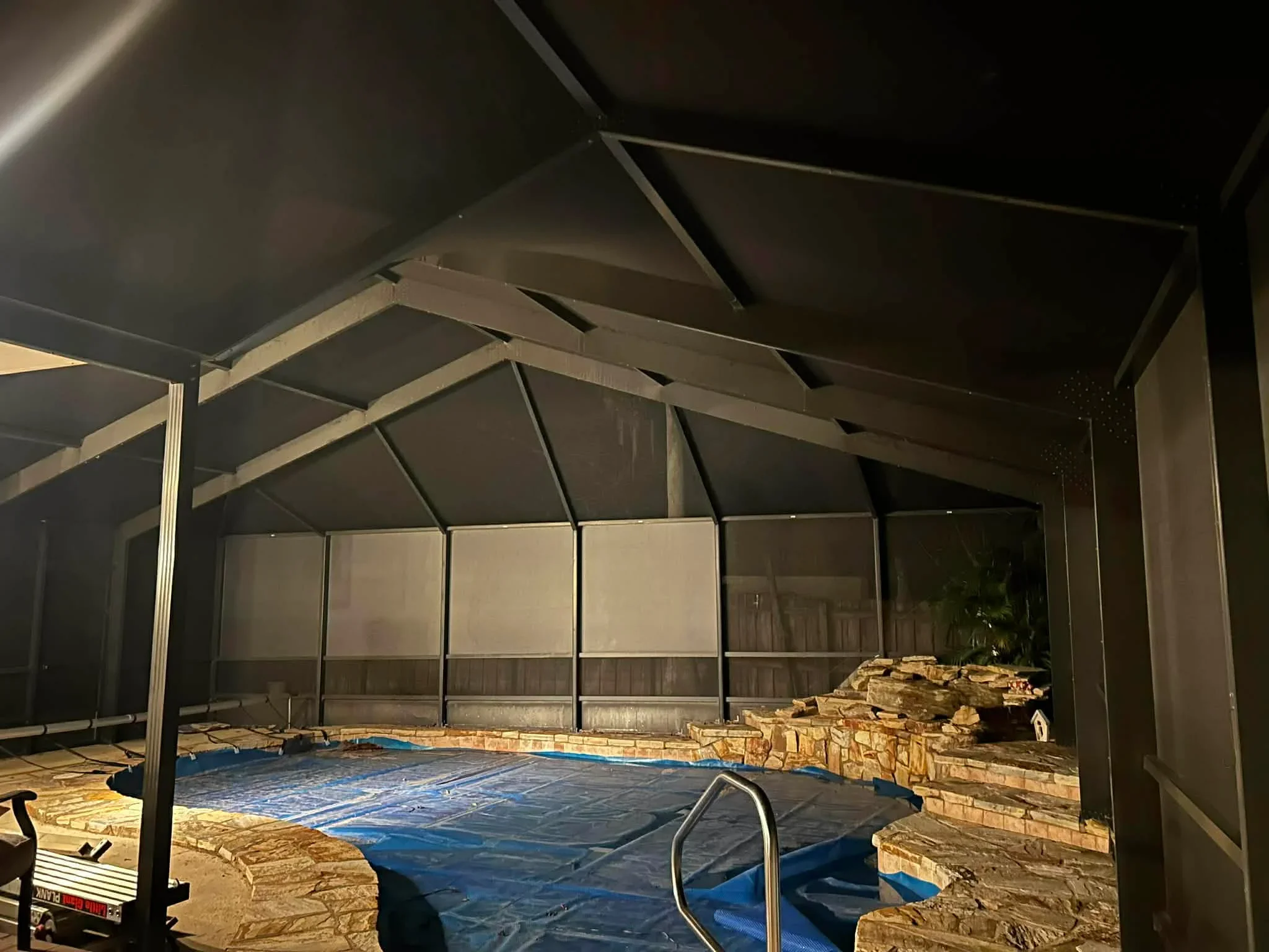Nighttime view of completed aluminum pool enclosure with mesh screening and peaked roof design