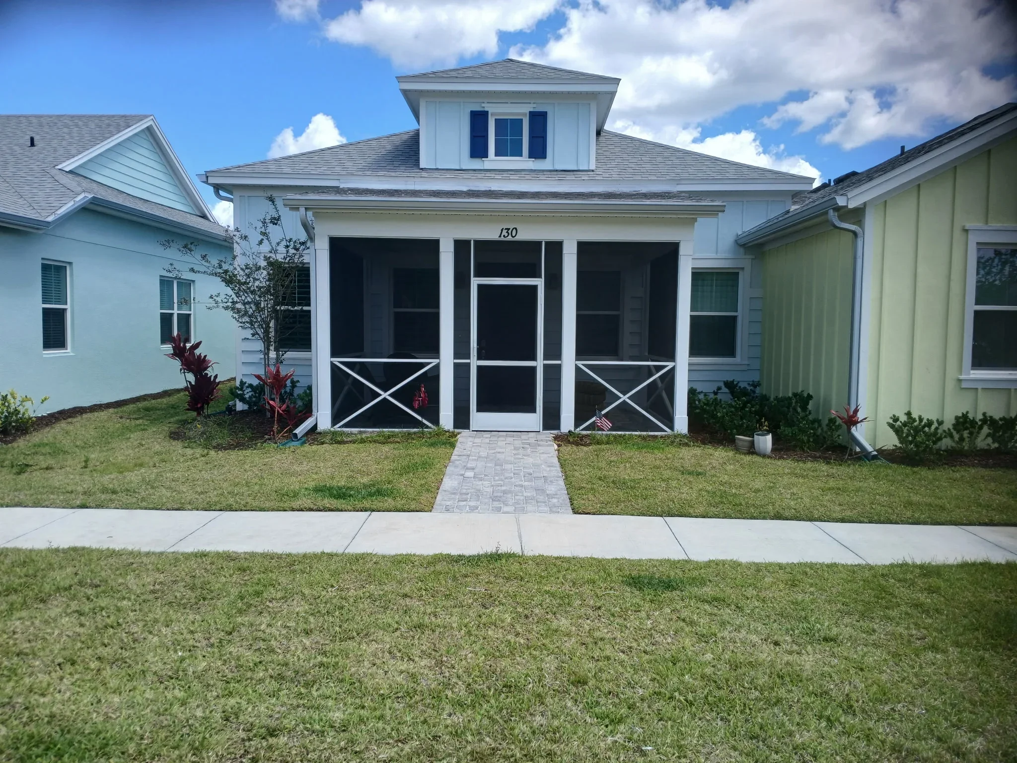 White cottage-style home with newly landscaped front yard, green sod, and red flowering plants