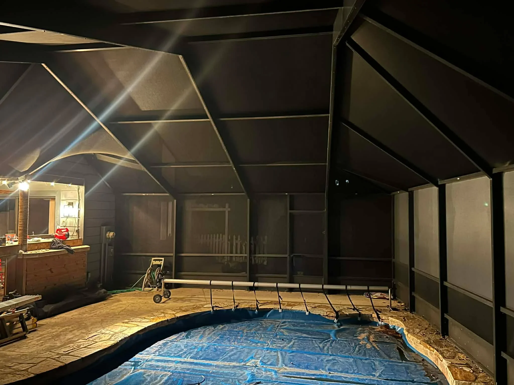 Nighttime view of completed black aluminum screen enclosure surrounding in-ground pool with peaked roof