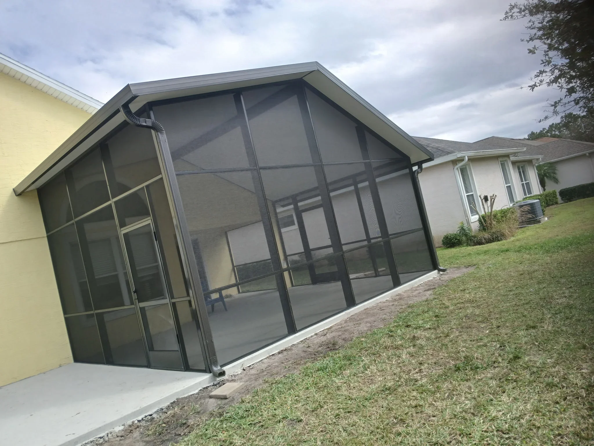 Charcoal gray aluminum screen porch enclosure with gabled roof attached to residential home