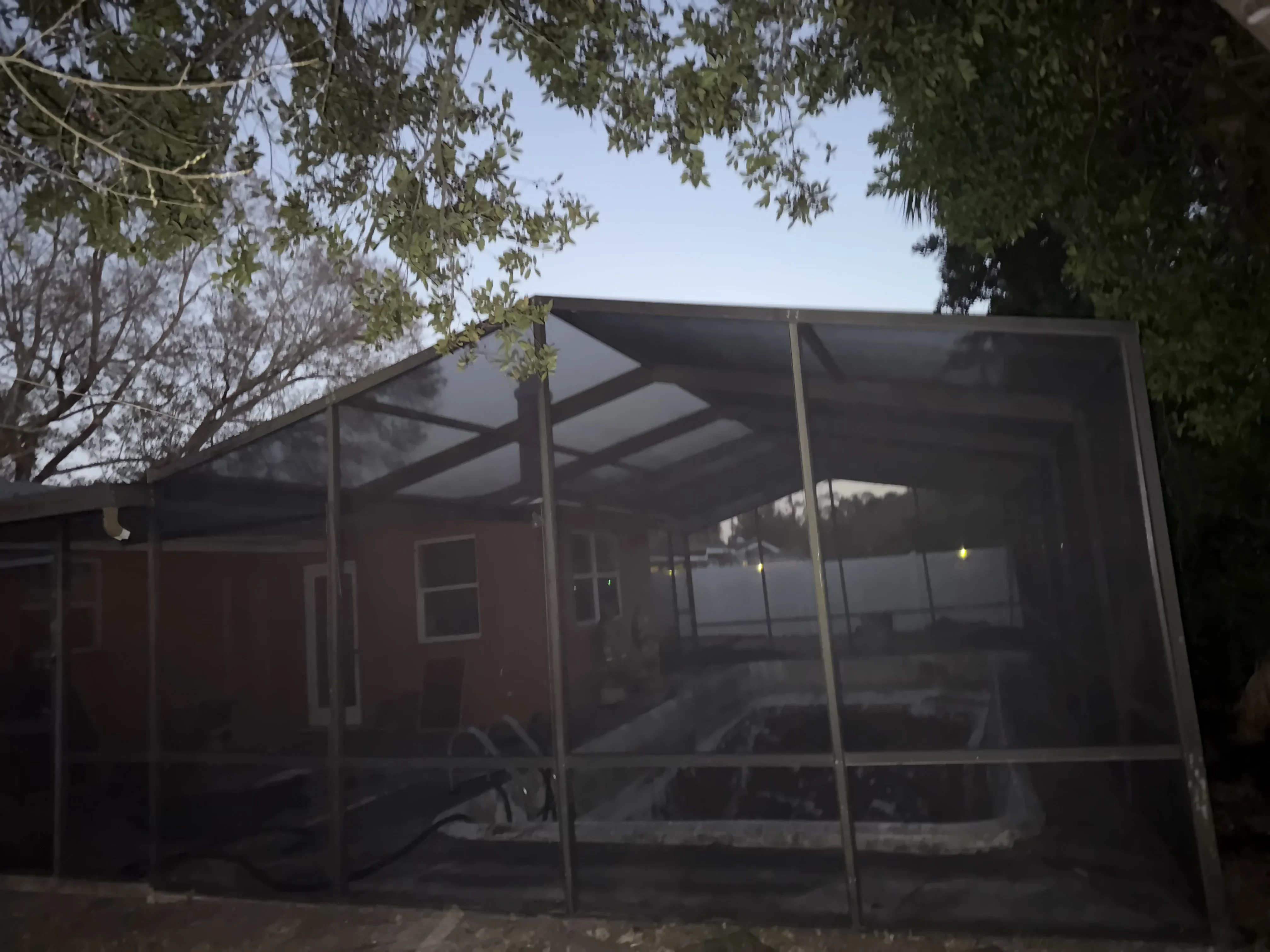 Aluminum-framed screen porch enclosure with dark mesh screening on brick home