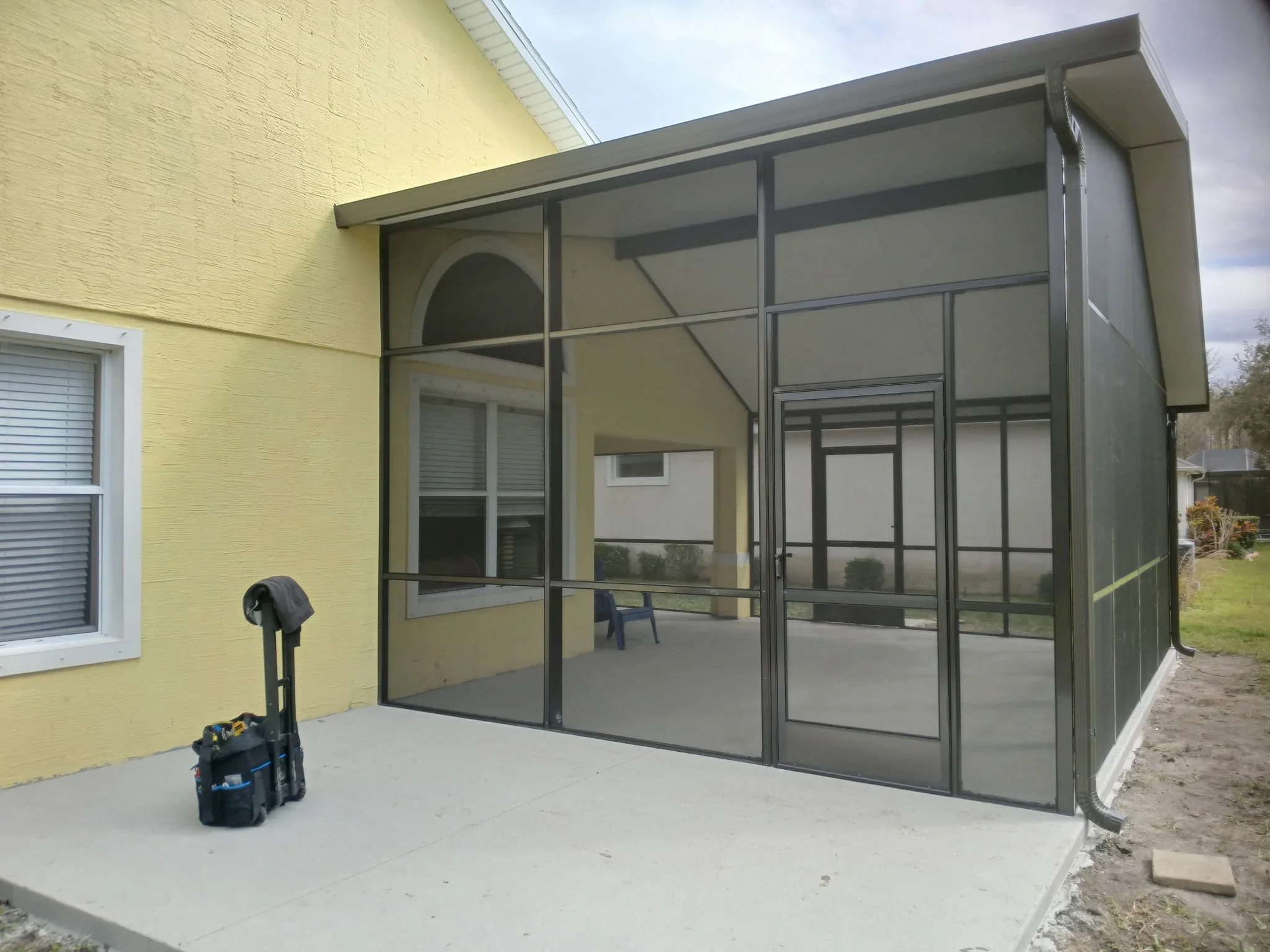 Aluminum screen porch enclosure with dark frame and full screening panels attached to yellow brick home