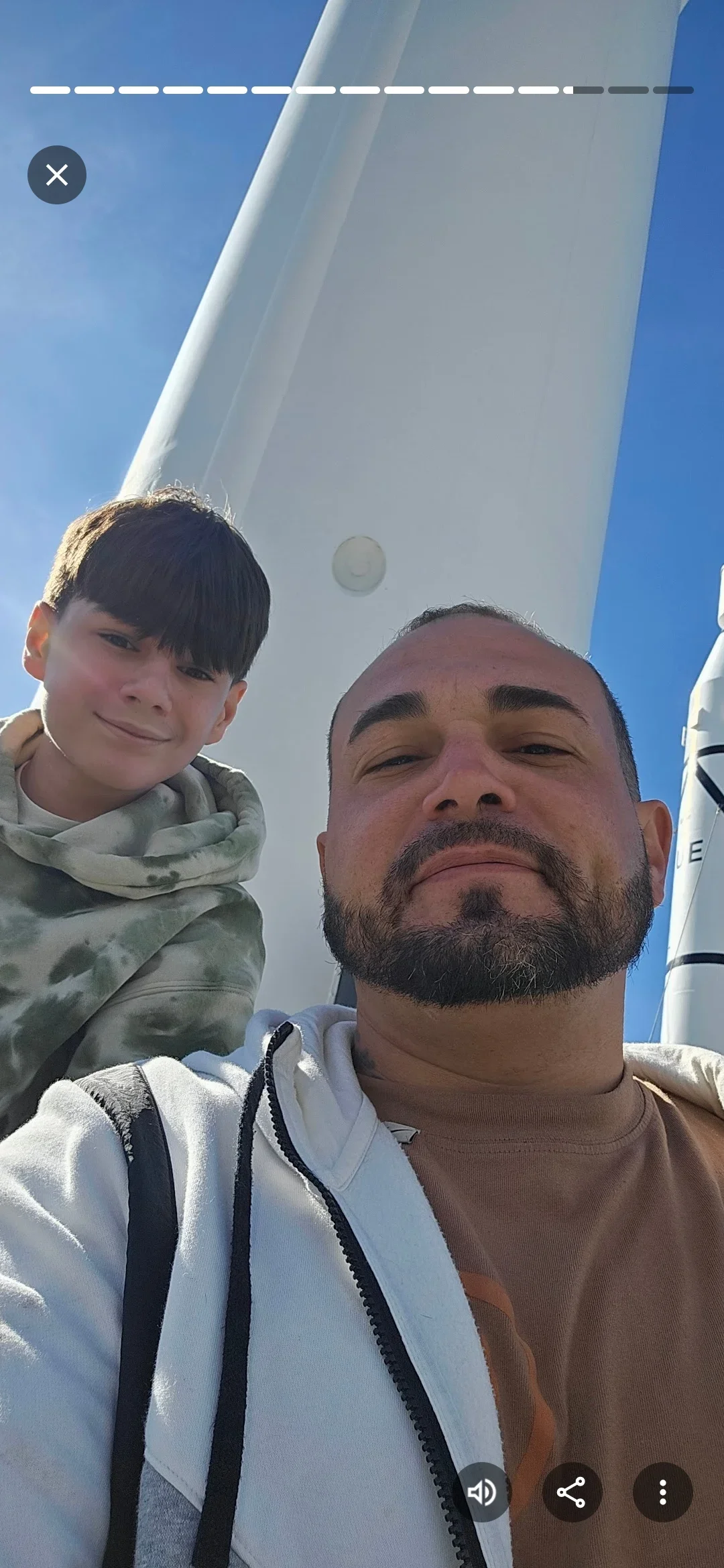 Two workers posing in front of tall white wind turbine tower against clear blue sky