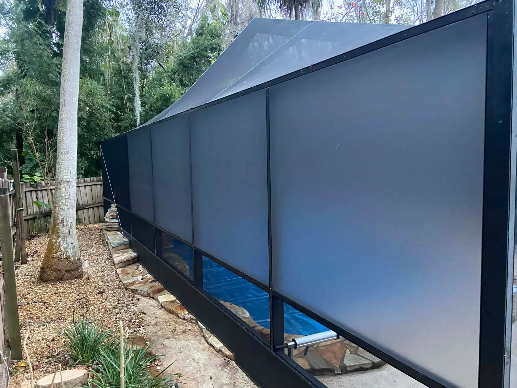 Black aluminum screen enclosure with pitched roof installed in backyard among tall trees