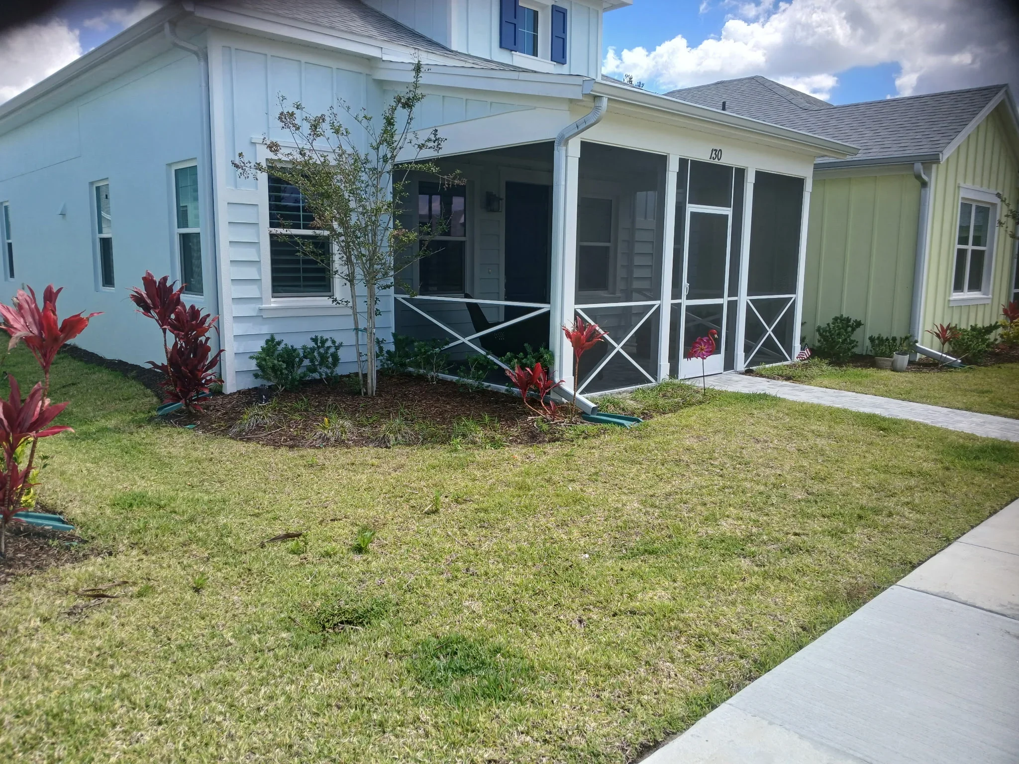 Light blue cottage with screened porch, new sod lawn, mulch beds with red flowers, and concrete walkway