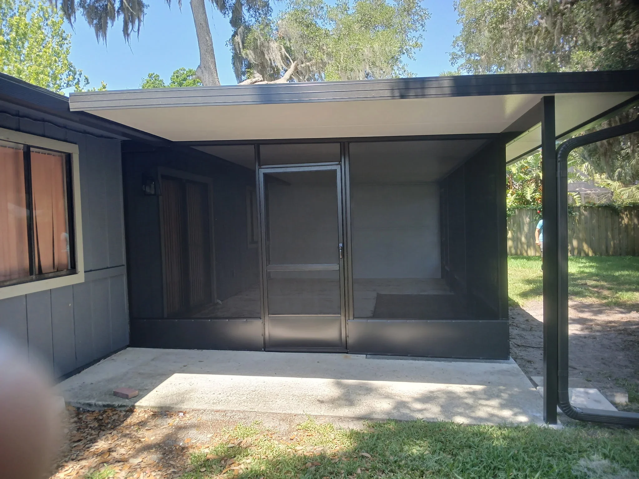 Gray aluminum screen enclosure with roof panel and glass doors on concrete patio